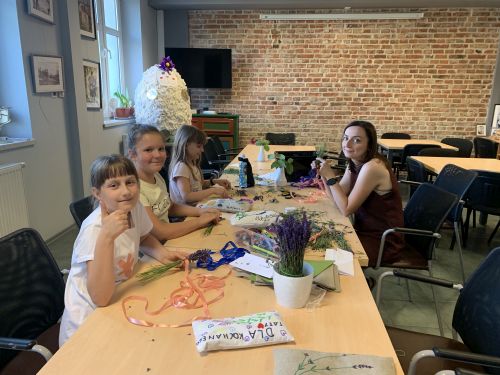 na zdjęciu widoczne kobiety w różnym wieku siedzące przy stole, na stole leżą kwiaty lawendy i przybory do warsztatów