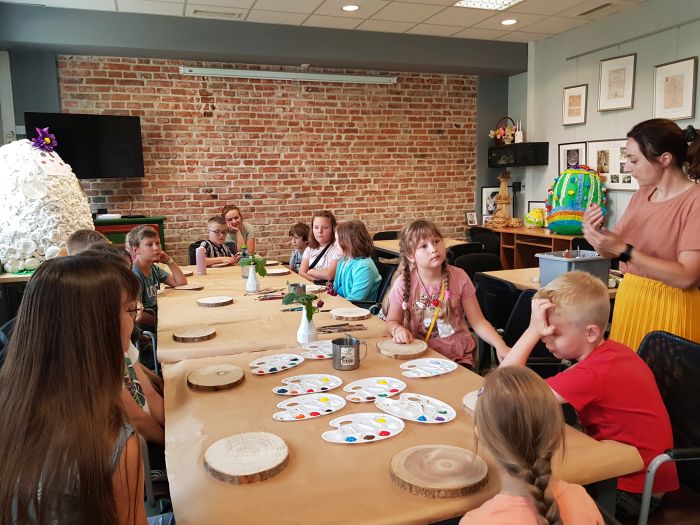 zdjęcie przedstawia dzieci siedzące przy stołach podczas warsztatów, na stółach przybory do malowania