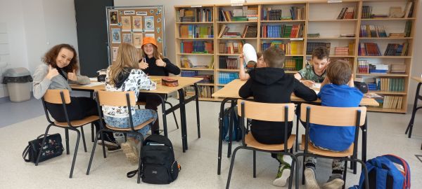 na zdjęciu widoczna grupa uczniów siedząca przy stolikach w bibliotece szkolnej
