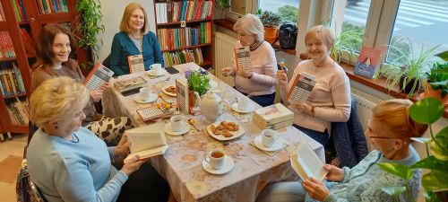 zdjęcie przedstawia grupę sześciu kobiet w różnym wieku siedzącą przy stole, w rękach trzymają książki