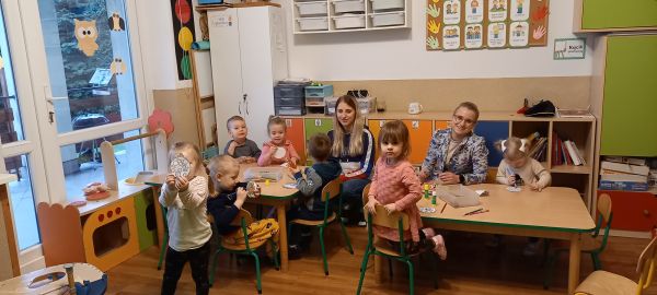 zdjęcie przestawia dzieci siedzące przy stolikach na zajęciach w przedszkolu