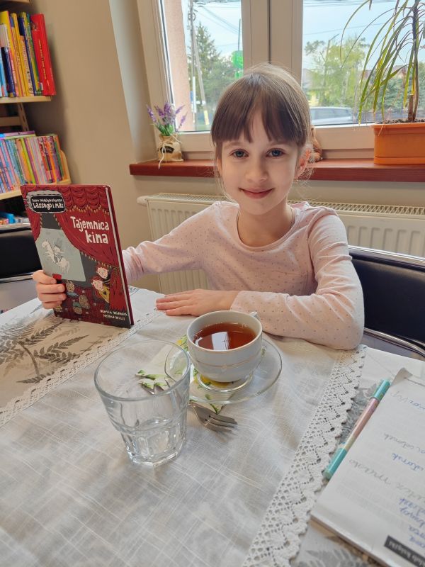zdjęcie przedstawia dziewczynkę siedzącą przy stole z książką