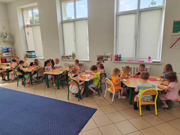 zjęcie przedstawia przedszkolaki siedzące przy stolikach podczas zajęć