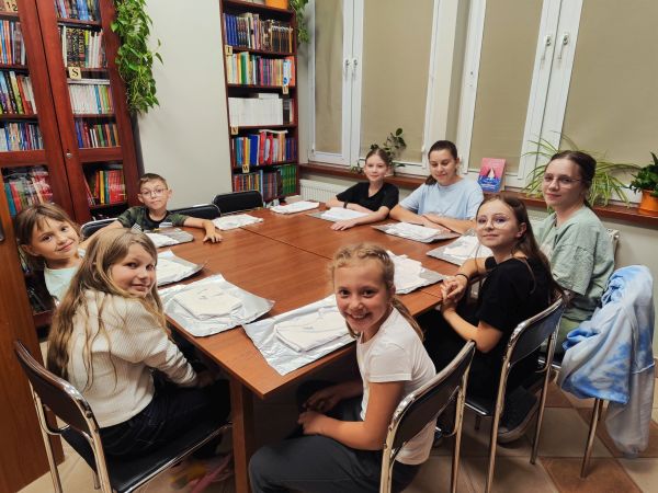 na zdjęciu widoczna grupa dzieci siedząca przy stole w bibliotece