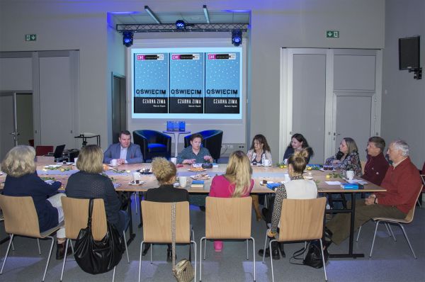zdjęcie przedstawia grupę osób siedzących przy stole podczas spotkania klubu dyskusyjnego