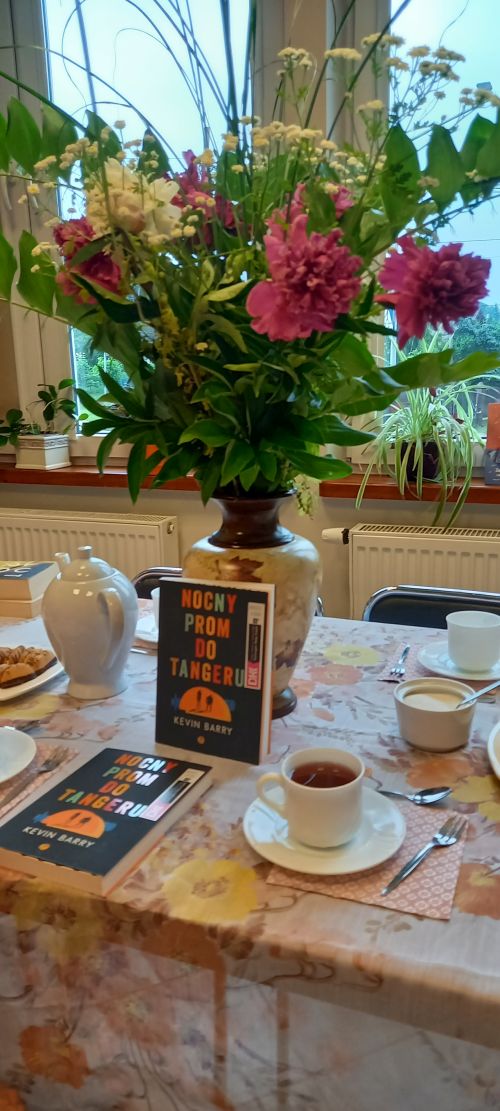 na zdjęciu widoczny wazon z kwiatami stojącymi na stole, pod wazonem książki
