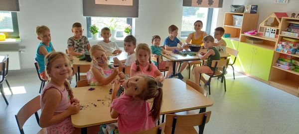 na zdjęciu widoczne dzieci siedzące przy stolikach wraz osobą dorosłą w sali szkolnej