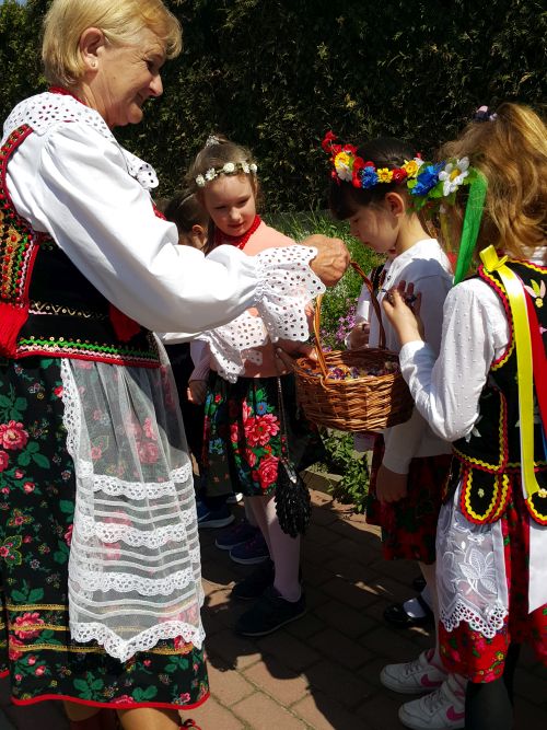 na zdjęciu widoczna kobieta w stroju krakowskim daje cukierki z koszyka dziewczynkom w strojach krakowskich