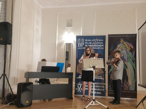 na zdjęciu widoczne dwoje dzieci grających na skrzypcach, w tle banery