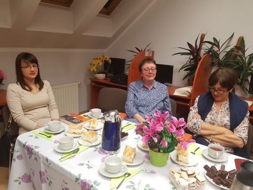 trzy kobiety siedzą przy stole, na stole filiżanki i ciasto