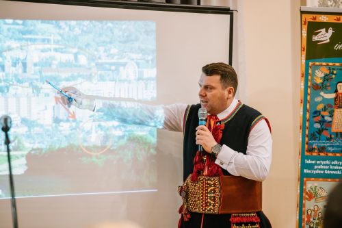 mężczyzna w stroju krakowskim wskazuje na coś na wyświetlanym na ekranie pokazie slajdów