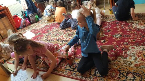 zdjęcie przedstawia dzieci siedzące na dywanie podczas kolorowania
