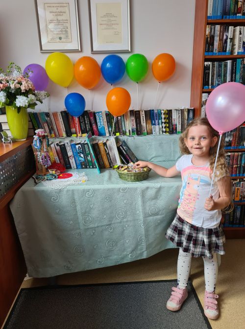 na zdjęciu widoczna dziewczyna stojąca z balonikiem w ręce w bibliotece