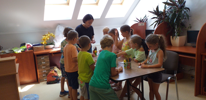 na zdjęciu widoczna grupa dzieci stojąca przy stole podczas zajęć plastycznych