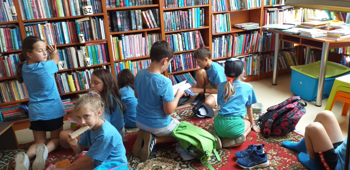 na zdjęciu widoczna grupa dzieci ogladająca książki w bibliotece