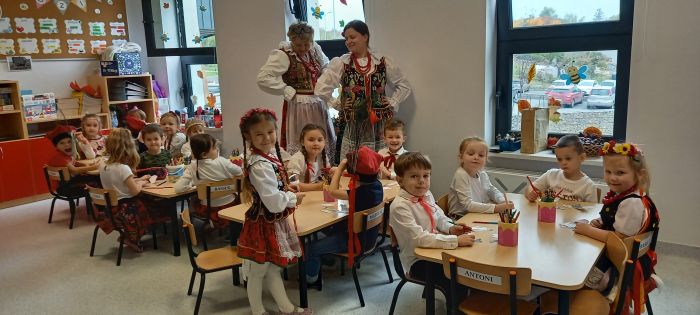 zdjęcie przedstawia dzieci siedzące w ławkach w sali przedszkola, część z nich ubrana jest w stroje krakowskie