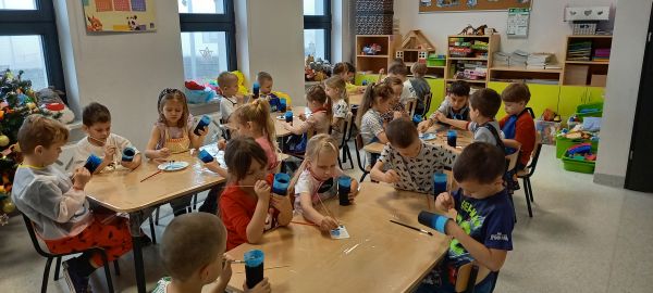 na zdjęciu widoczne przedszkolaki siedzące przy stolikach podczas zajęć