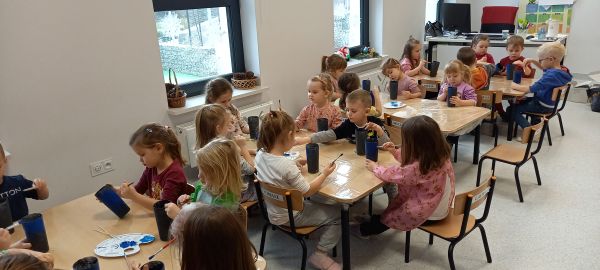 na zdjęciu widoczne przedszkolaki siedzące przy stolikach podczas zajęć