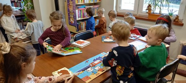 zdjecie przedstawia przedszkolaki w sali bibliotecznej oglądające książki