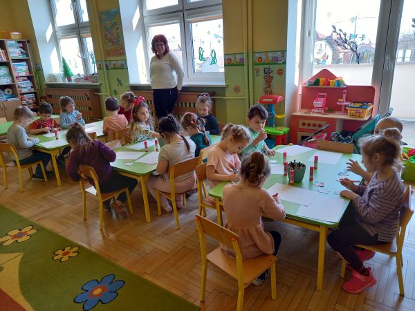 zdjęcie przedstawia przedszkolaki siedzące przy stolikach podczas zajęć