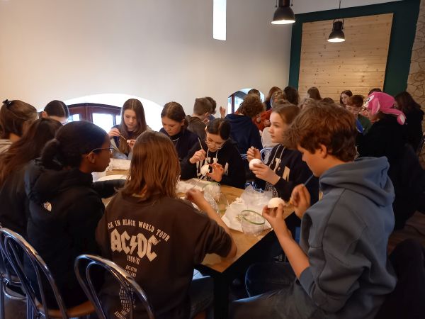 na zdjęciu widoczna grupa uczniów siedząca lub stojąca wokół stołów podczas zajęć