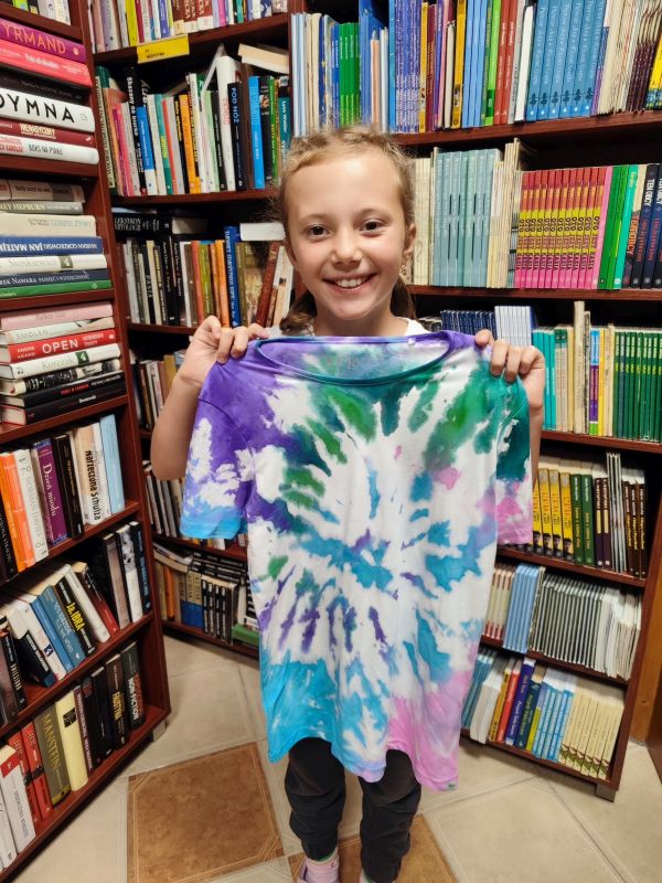 zdjęcie dziewczynki trzymającej ozdobioną koszulkę przed sobą na tle regałów bibliotecznych