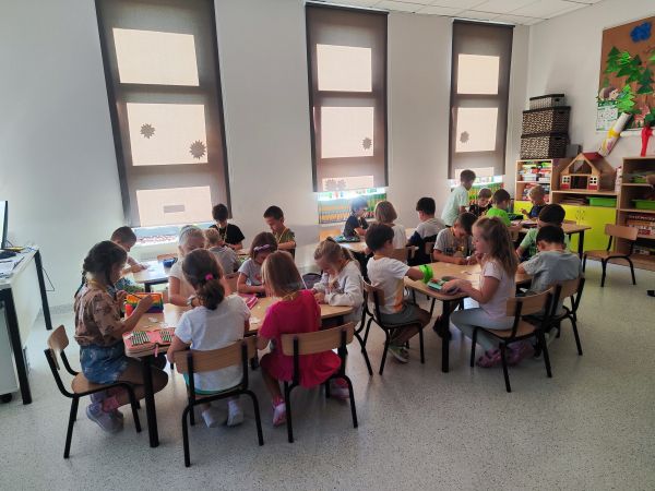 zdjęcieprzedstawia przedszkolaki siedzące przy stolikach podczas zajęć