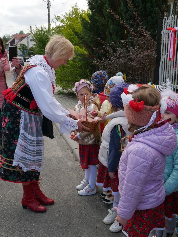zdjęcie przedstawia kobietę w stroju krakowskim dającą cukierki przedszkolakom z koszyka