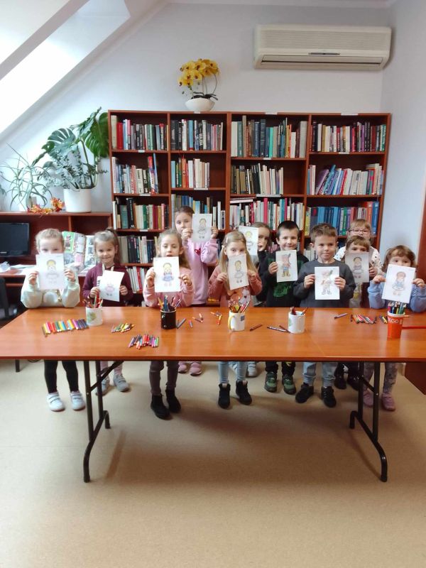 zdjecie przedstawia grupę przedszkolaków  w bibliotece z przygotowanymi przez siebie pracami