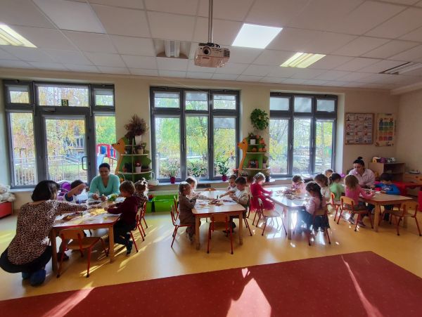 zdjęcie przedstawia dzieci siedzące przy stolikach w przedszkolu