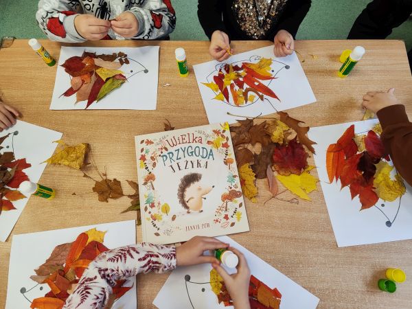 zdjęcie przedstawia książkę leżącą na stoliku przy którym dzieci wykonują pracę z liści